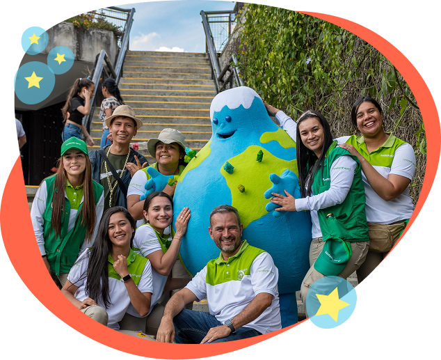 nuestros-eventos Niños sentados observan a un personaje animado azul en una actividad infantil frente a la Casa de la Música, acompañado por dos guías.